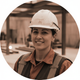Smiling female construction worker in a hard hat, a construction site blurred in the background.